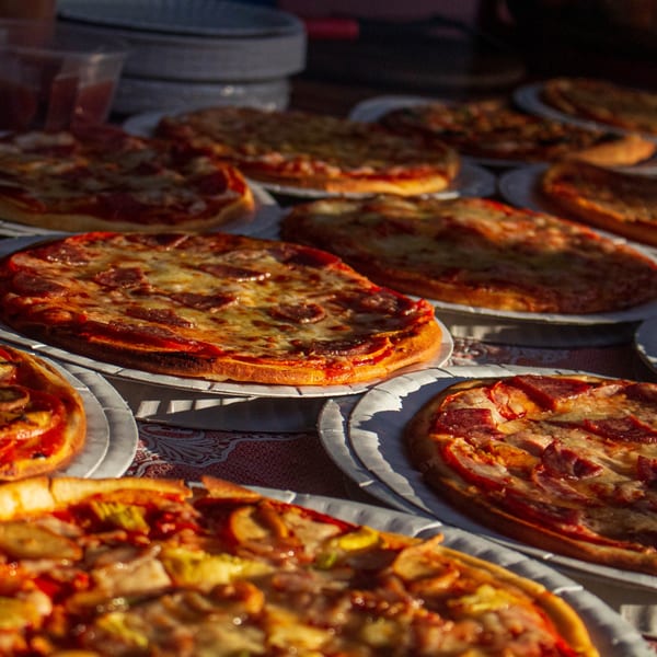 Multiple small, round pizzas with various toppings, including pepperoni, on white paper plates.
